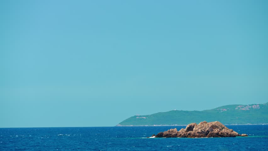 rocky shore of Adriatic Sea, against background of blue water and sky to horizon, mountains covered with trees, abstract backdrop of summer travel and vacation