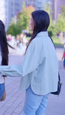 Two young asian women hugging and smiling while taking a selfie with a smartphone outdoors