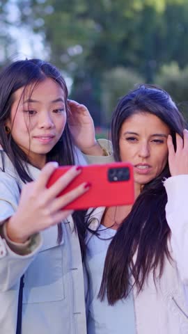 Happy multiracial lesbian couple taking a selfie with a smartphone and hugging with love in a park