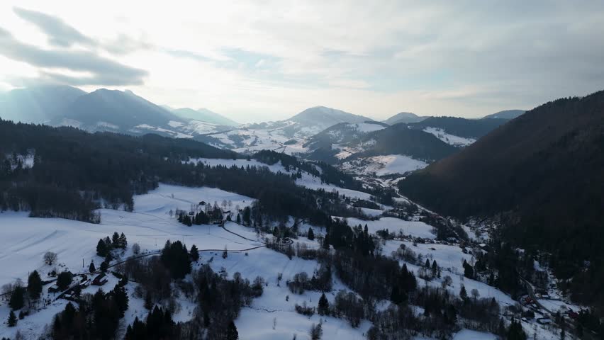 Aerial sideways view of winter mountain landscape with snow covered hills and rural valley