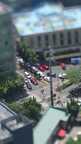 A 4K miniature effect (tilt-shift) video of the urban scene in Makati City, Metro Manila, Philippines. High angle view from a low-rise building showing buildings and street activity like a tiny toy world. Real-time footage, authentic city atmosphere.
