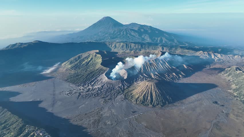Twin plumes rise from Bromo craters, the perfect cone dwarfed by rugged ridges under an endless East Java sky