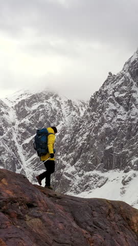 Side view of hiker with backpack walking in deep snow using trekking poles in alpine mountains. Adventurer moving through cold winter landscape during expedition with minimal environment and dramatic