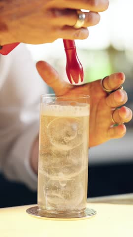 Professional bartender preparing a refreshing alcoholic beverage. The mixologist skillfully adds whipped cream foam to a sparkling drink