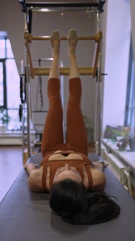 Woman hanging upside-down gripping pilates bar in large studio, working on advanced balance. Upside-down, pilates bar, advanced, balance, studio.