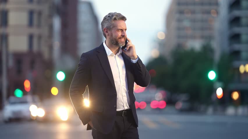 Business man communicating by phone in busy urban traffic. Corporate businessman on phone during evening city lifestyle. Business man talking on mobile phone while walking downtown.