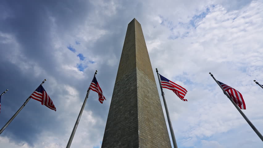 American flags surrounding historic Washington Monument. National memorial representing United States history. Patriotic architecture in Washington DC. Iconic obelisk with waving American flag.