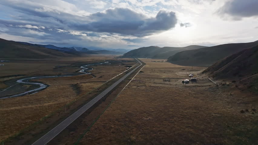 Aerial view of straight road and meandering rivers in Western Sichuan: Nomadic pastures with grazing yaks under the sunset on the Tibetan Plateau