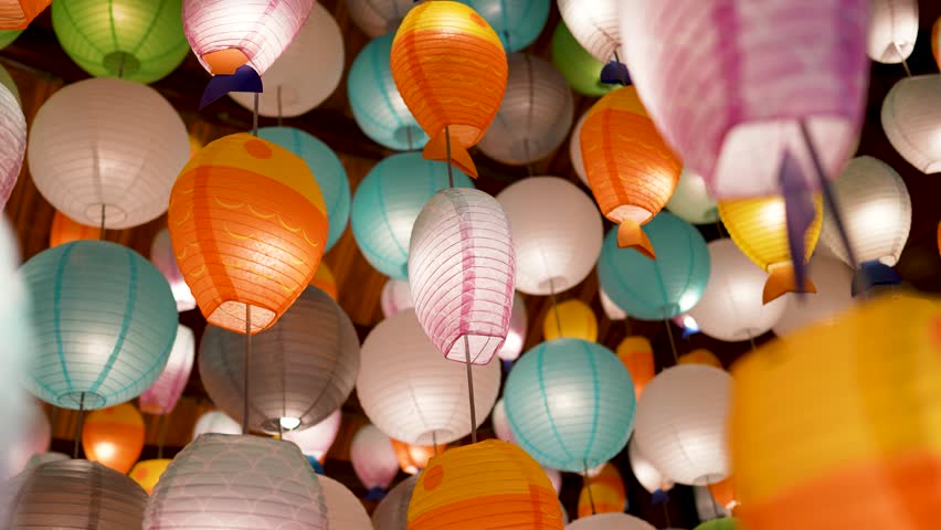 Many colorful glowing paper lanterns hanging from ceiling indoors. Electrical round and fish-shaped handmade paper lanterns garlands used as popular decoration for streets and indoor areas in Vietnam.