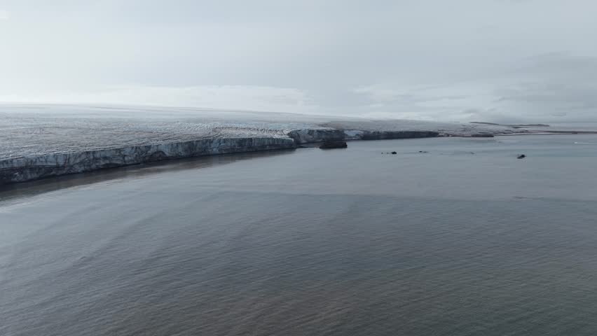 Cinematic aerial moving forward and raising to reveal the vast, crevassed surface of the Rotch Dome ice sheet and the dark volcanic shoreline of Elephant Point on Livingston Island
