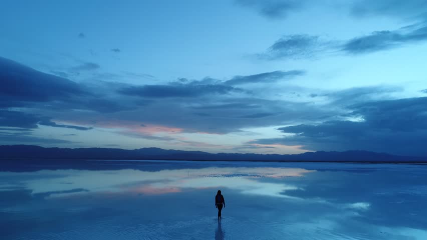 Aerial view of lone person walking on Chaka Salt Lake during blue hour sunset, reflection of sky.