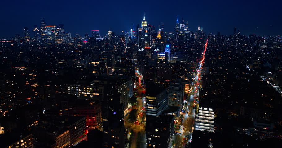 Well-illuminated streets of New York at night time. Drone flight over the dazzling panorama of Big Apple.