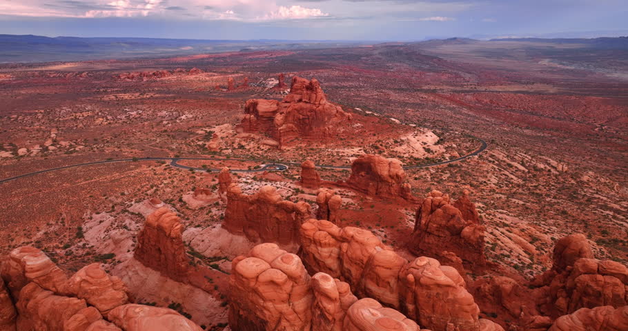 Deserted land with red ground and rocks. Drone flight approaching the wavy highway crossing the landscape of the Arches National Park, Utah, USA.