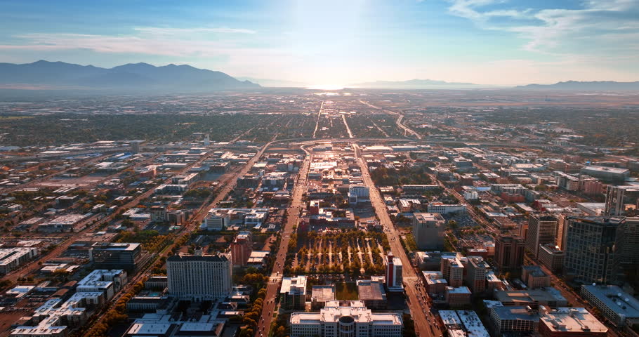 Straight parallel roads cross the urban landscape of the large city. Mountain silhouettes surround the territory of Salt Lake City, Utah, USA. Aerial view.