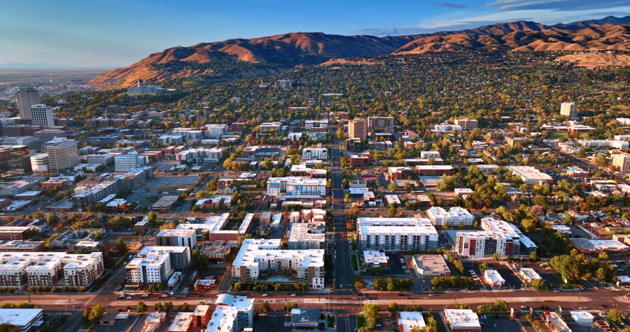 Lively green city scattered at the mountain foot. Drone footage above the cityscape of Salt Lake City, Utah, USA at sunset.