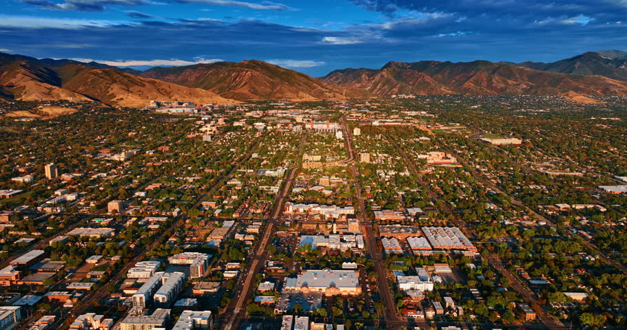 Beautiful green cityscape with low buildings in the cozy neighborhoods. Bright setting sun lights the bare rocks at backdrop. Salt Lake City, Utah, USA at sunset.