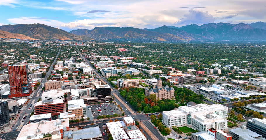 Flight over the green city surrounded by the beautiful rocks. Aerial perspective on Salt Lake City, Utah, USA at daytime.