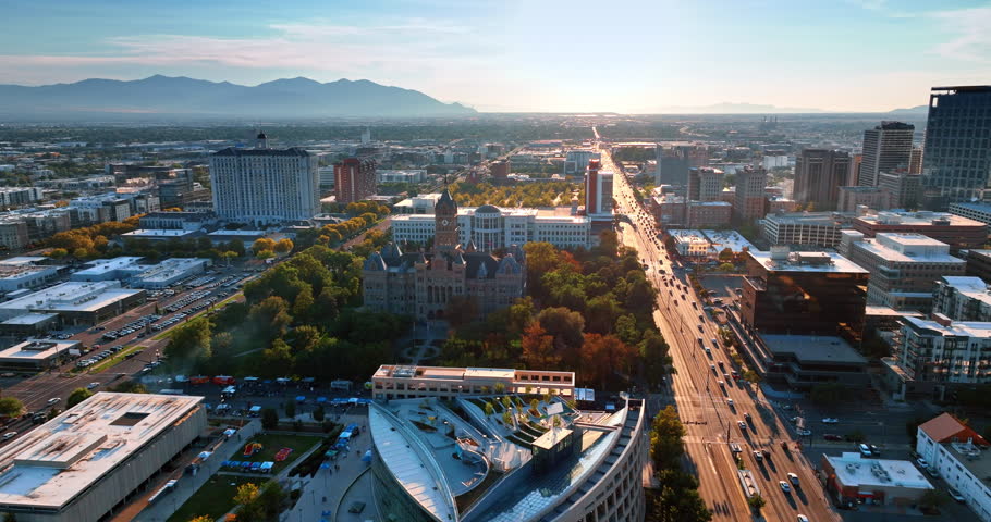 Flying to the beautiful Salt Lake City and County Building in Salt Lake City, Utah, USA. View on the sunlit road with multiple moving cars at sunset.