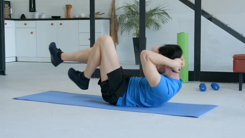 Motivated sporty fit senior man practicing bicycle crunches exercise on yoga mat, flexing and strengthening abdominal muscles and slimming waist during sports training at home.