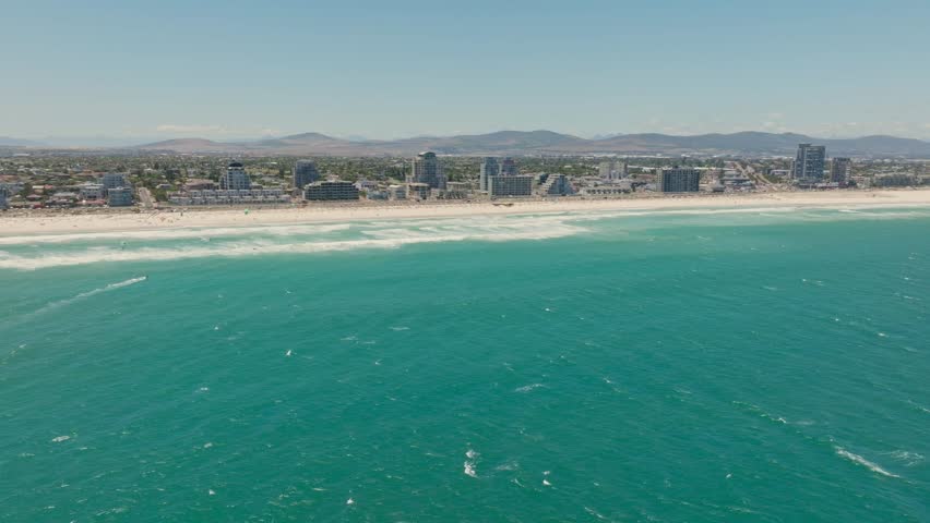Aerial view of Bloubergstrand beach and Cape Town skyline with waves crashing on white sand in South Africa