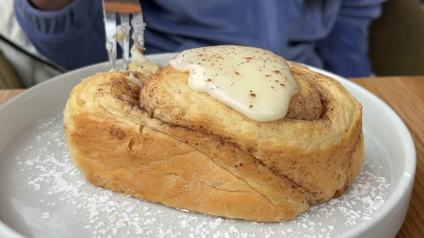 Tasty cinnamon roll with creamy glaze, powdered sugar on plate, homemade bakery concept.