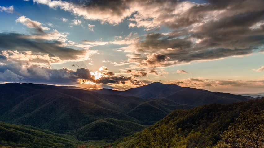 Sunlight breaks through dramatic clouds over rolling green mountain ridges during sunset in scenic blue ridge parkway