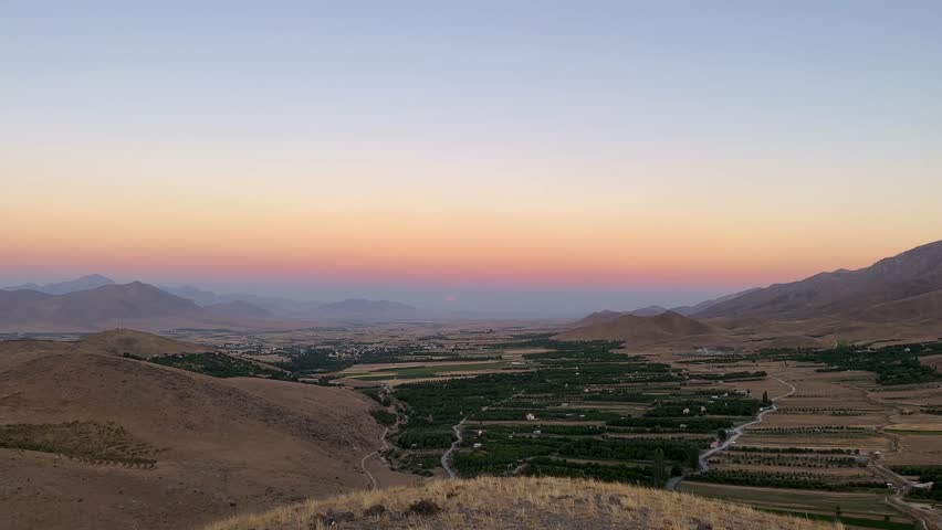 Panoramic view of mountain valley at sunset with vibrant orange sky and full moon rising