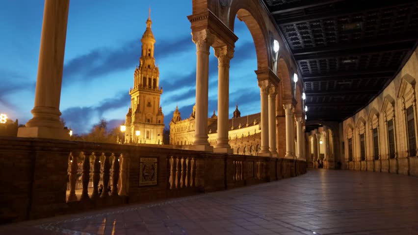 Night view of Plaza de Espana in Seville through gallery of columns, illuminated landmark under blue twilight sky. Plaza de Espana during blue hour in Seville