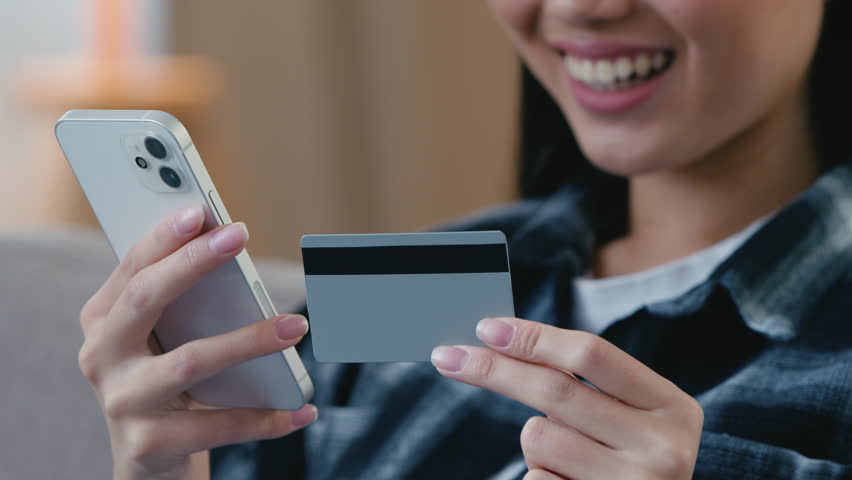 Glad joyful unrecognizable Asian woman paying online mobile phone holding bank credit card making internet payment Korean Japanese female girl hands purchase buying in shopping app digital transaction