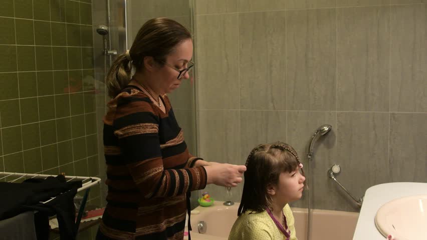Mother braiding daughter hair in bathroom during morning routine
