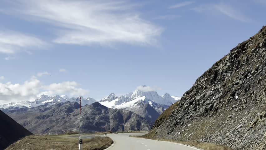 Mountain highway curving through a vast alpine pass, showing open-road freedom, dramatic peaks, and classic self-drive travel.