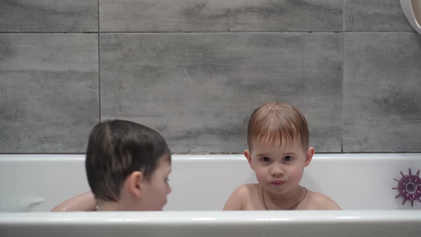 Two little boys having fun while taking bath in bathtub. Little children playing in the bath during the bathing.