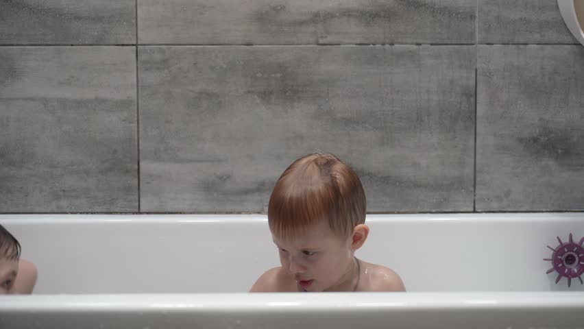 Two little boys having fun while taking bath in bathtub. Little children playing in the bath during the bathing.