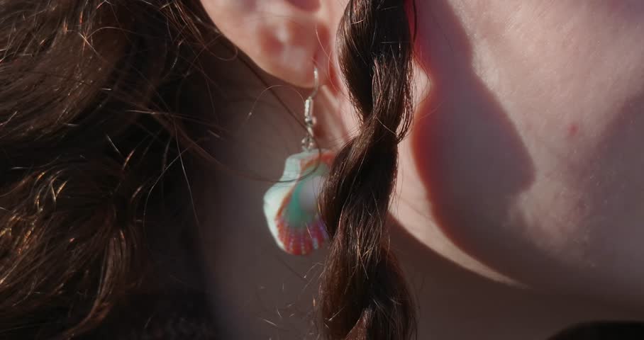 Close-up of woman ear with colorful shell earring in warm sunlight, lifestyle detail