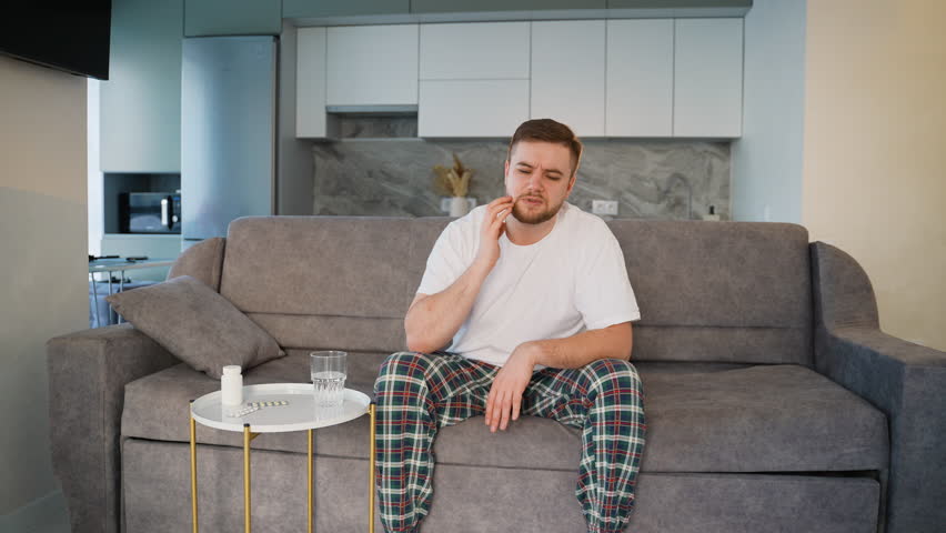 Young man in pajamas suffering from severe toothache at home