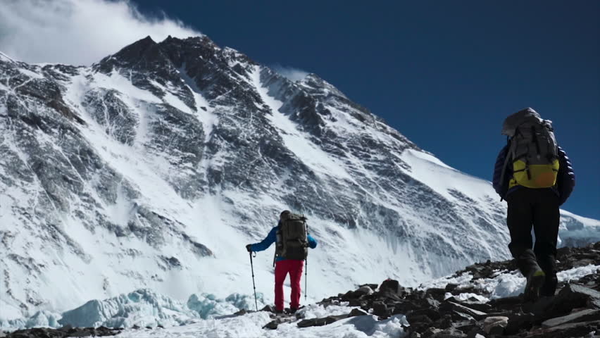 Pair of mountaineers with backpacks trekking in the Himalayas, climbing towards a snowy mountain peak