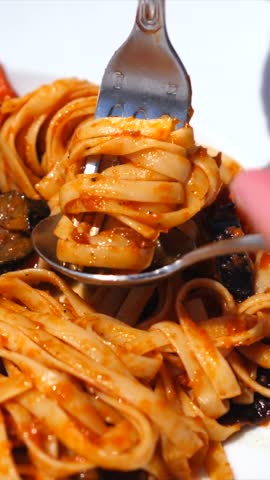 Close up of a person twirling fresh linguine with tomato sauce onto a fork with the help of a spoon. This traditional italian dish represents a classic and delicious culinary experience