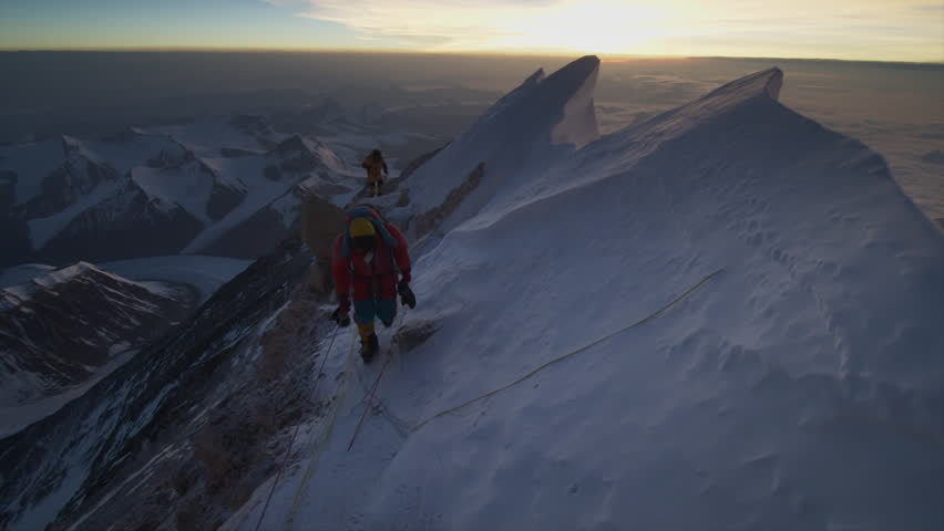 Alpinists climbing a narrow snowy ridge on Mount Everest with a stunning sunrise in the background