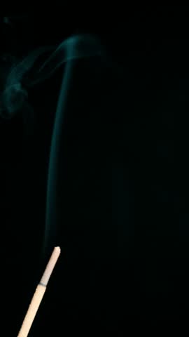 Vertical shot of aromatic incense stick with teal smoke on black