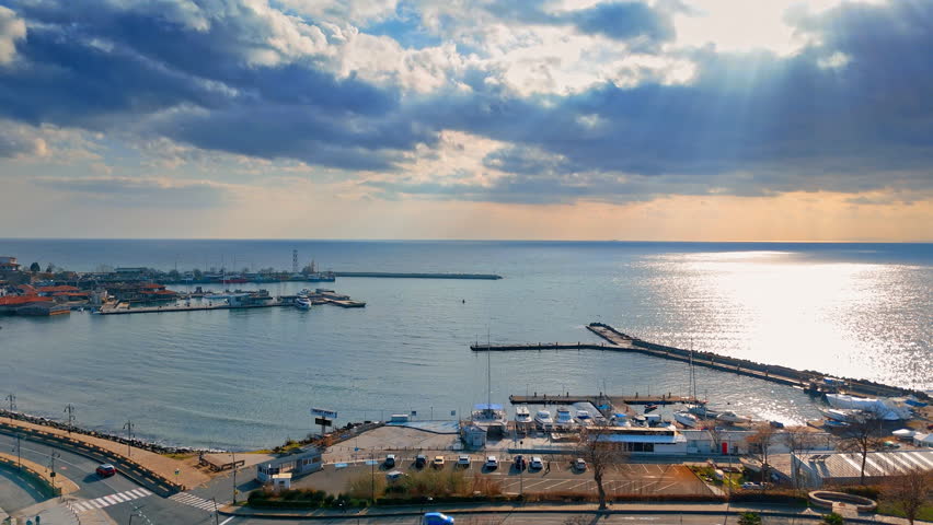 Seascape with harbor piers and boats under dramatic cloudy sky. Coastal view of a marina with docks and reflections on the water surface during late afternoon.
