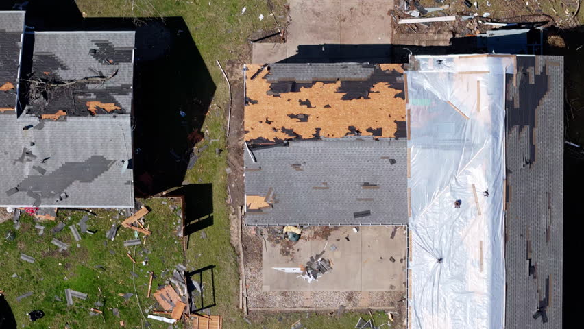 Top down aerial view of residential neighborhood destruction after a tornado with damaged roof of houses and scattered debris.