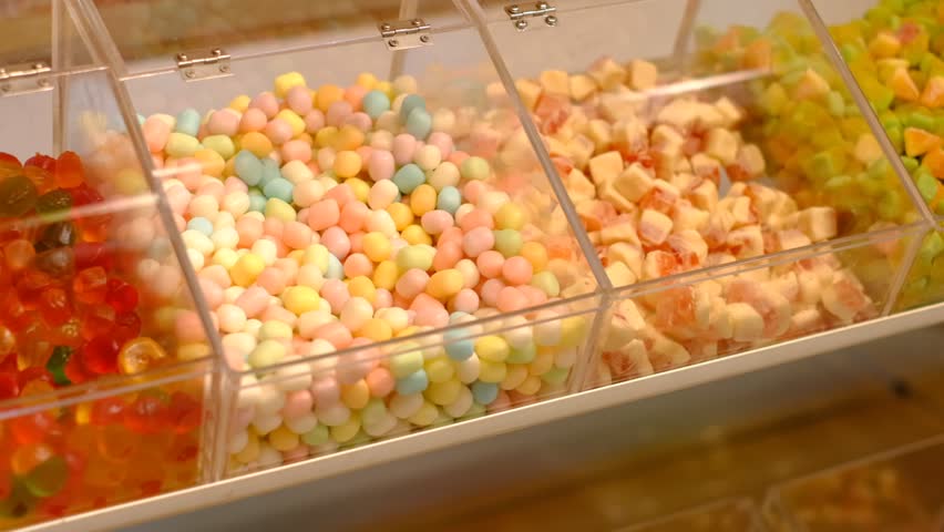 A container of jelly beans is on a shelf with other containers of candy. The jelly beans are in different colors and shapes, and they are all piled up in the containers