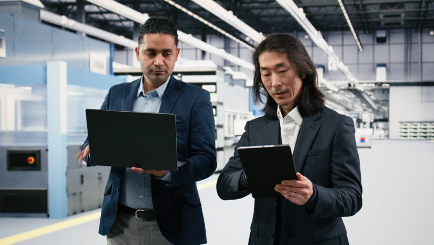 Microchips manufacturing plant multiethnic engineering team tracks semiconductor fabrication. Multiracial teamworking colleagues in PCB production factory oversee infrastructure with devices, camera B