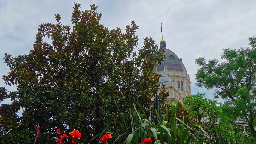 Scenic view of the Royal Exhibition Building dome emerging through lush garden foliage and flowers in Melbourne. Framed by trees and greenery under soft daylight, capturing heritage architecture and urban nature.
