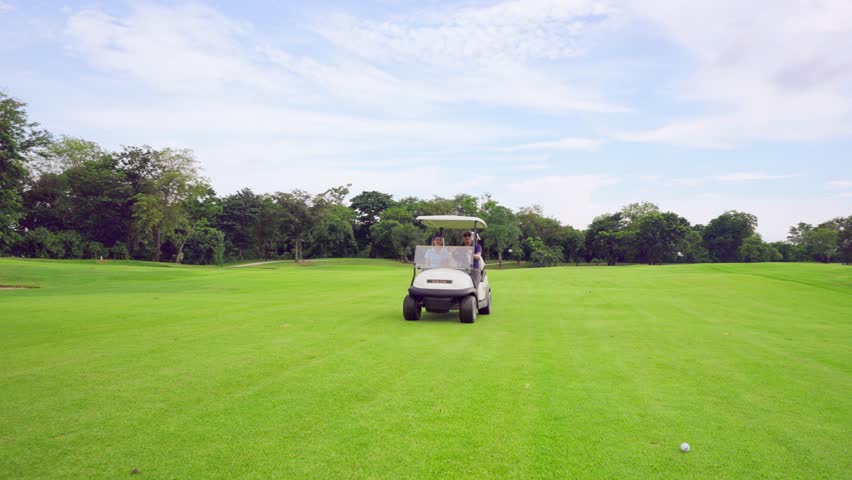 Asian golfer team ride in golf cart together on a scenic golf course. Active young sport people enjoy fun game outdoor recreation, leisure lifestyle and light exercise while drive through the field.