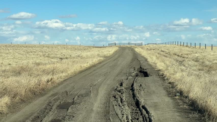 Driver POV on rural dirt road through open countryside landscape with natural terrain and wide horizon
