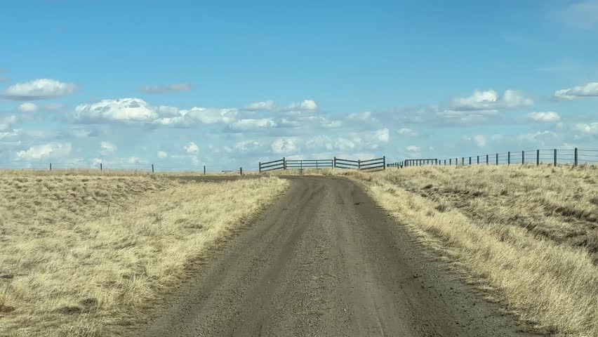 Driver POV on rural dirt road through open countryside landscape with natural terrain and wide horizon