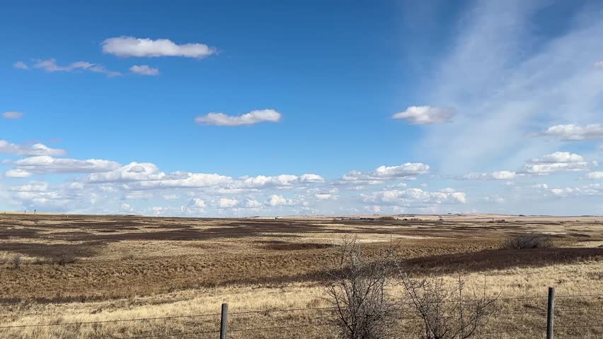 Vast prairie landscape with dramatic cloud formations and distant mountain horizon under bright sky
