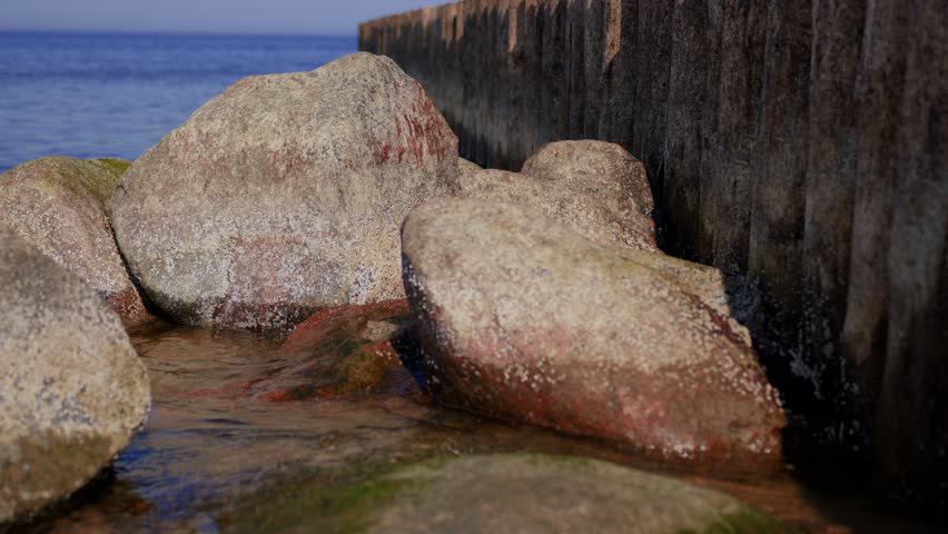 Sea waves washing over stony beach with wooden pier. Coastal landscape with rocky shore, water movement and structure. Summer seascape scene by seaside nature.