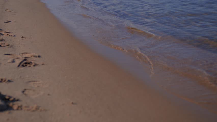 Gentle ocean waves lapping against the sandy shore at the beach. Transparent water flowing over wet sand. Serene coastal landscape during a calm summer day.